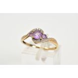 AN AMETHYST AND DIAMOND RING, the yellow metal ring of cross over design, set with three graduated