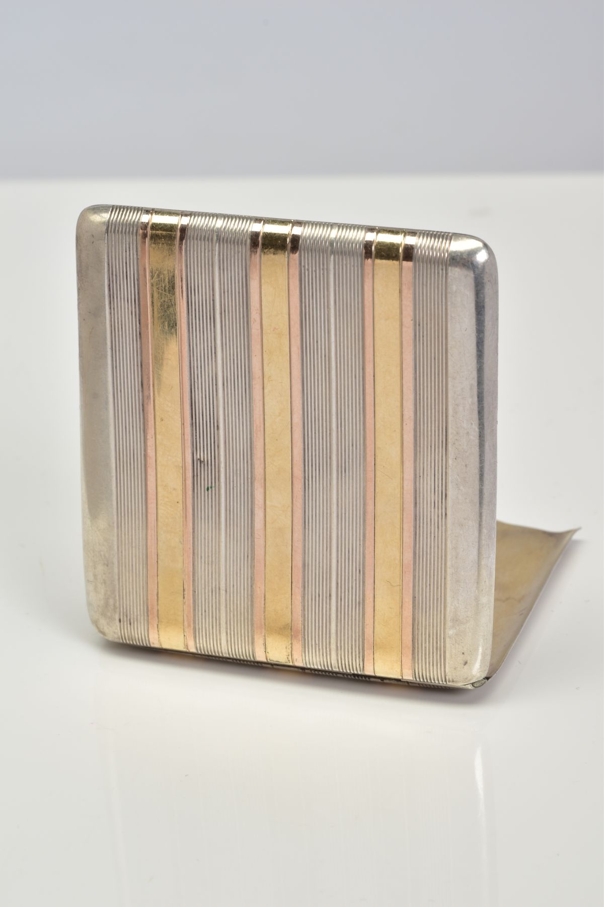 A WHITE METAL CARD CASE, the hinged case designed with white and yellow metal engine turn pattern to