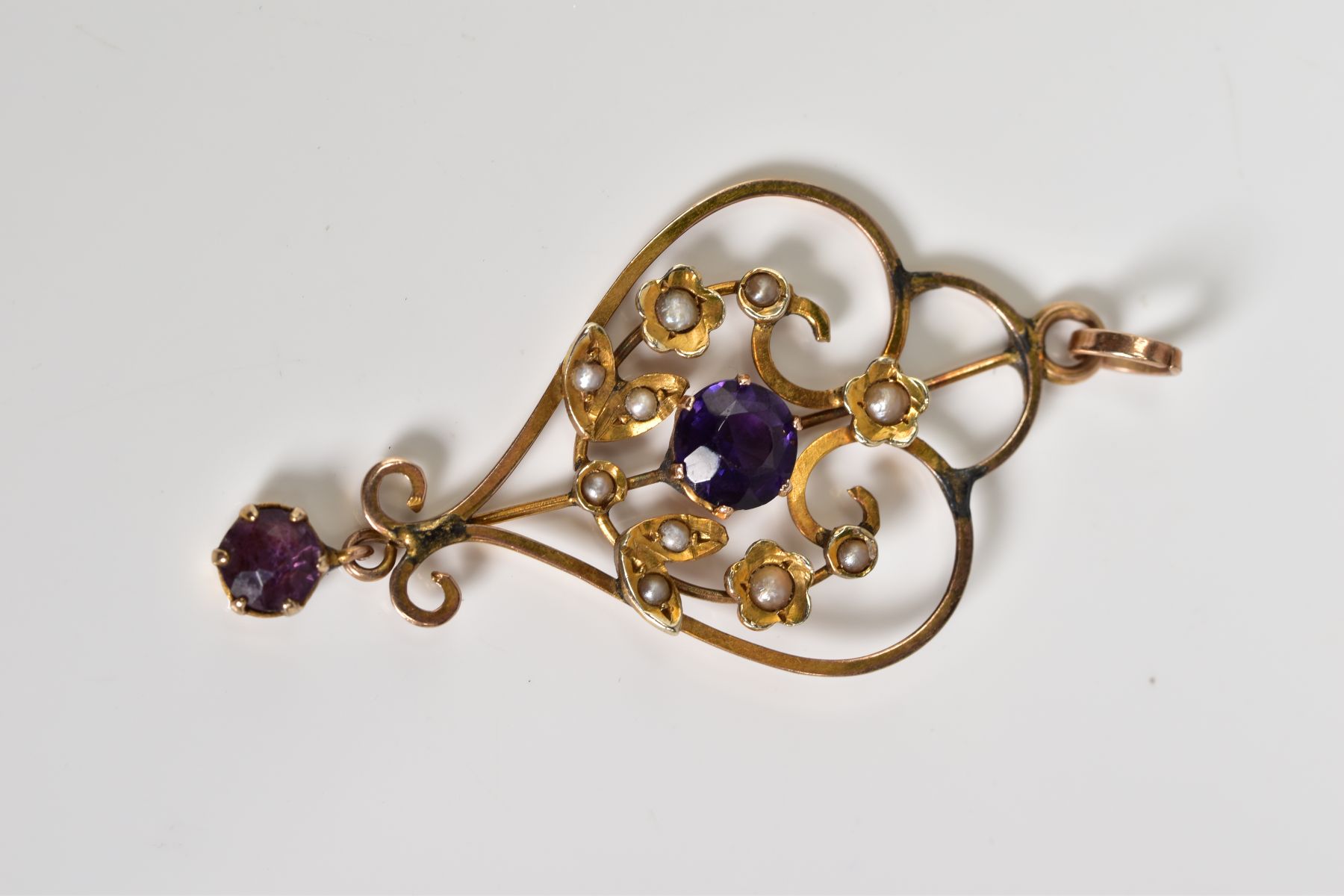 AN EDWARDIAN YELLOW METAL BROOCH, of openwork design, central panel set with a purple garnet