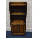 LIBERTY, BIRMINGHAM, a slim mid 20th century oak triple tier bookcase above double panel fall