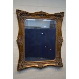 A LARGE MID TO LATE 20TH CENTURY HEAVILY FOLIATE GILT WOOD FRAMED BEVELLED EDGE WALL MIRROR, 136cm x