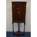 A GEORGIAN OAK BOWFRONT TWO DOOR CORNER CABINET on a stand, turned front legs united by an