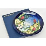 A BOXED MOORCROFT POTTERY PLATE, 'Sweet Betsy' pattern on blue ground, impressed backstamp,