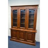 A STAINED PINE GLAZED TRIPLE DOOR BOOKCASE above triple panelled doors, width 180cm x depth 50cm x