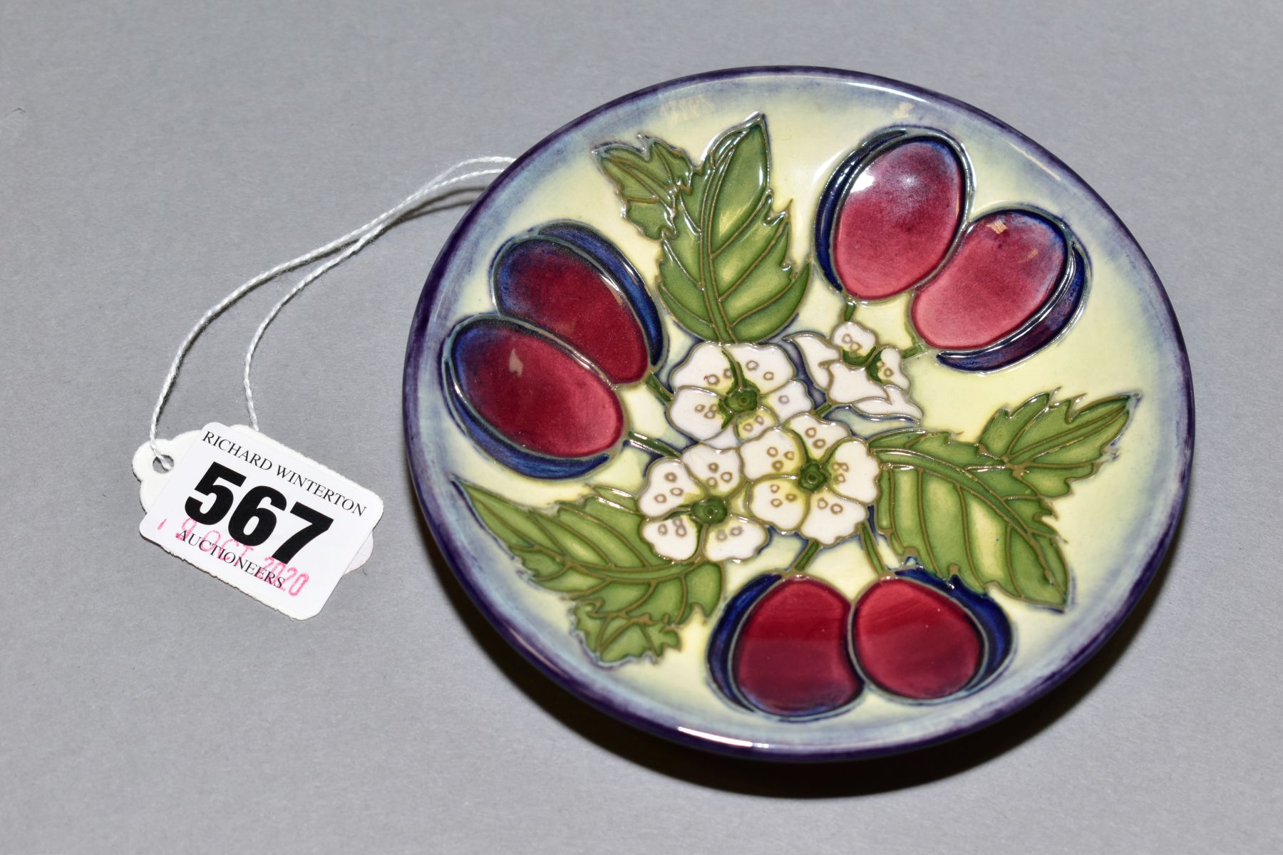 A MOORCROFT CIRCULAR COASTER DECORATED IN THE PLUMS AND BLOSSOM PATTERN, marked with 'T' as a