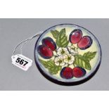 A MOORCROFT CIRCULAR COASTER DECORATED IN THE PLUMS AND BLOSSOM PATTERN, marked with 'T' as a