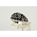 A GEM SET RING, the white metal ring designed with an oval panel set with circular cut black