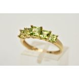 A 9CT GOLD PERIDOT RING, designed with a tiered row of claw set, square cut peridots, to a plain