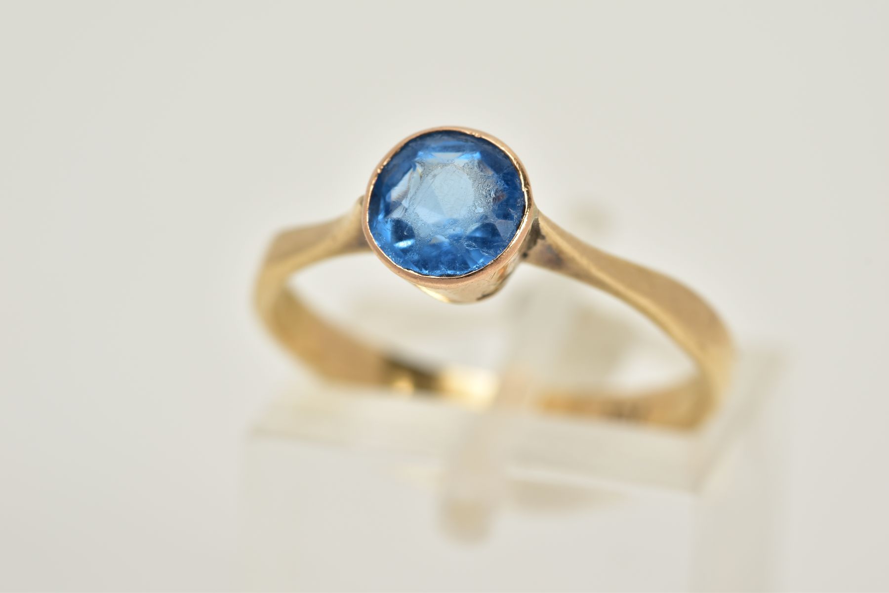 A YELLOW METAL GEM SET RING, set with a circular cut blue stone assessed as paste, tapered