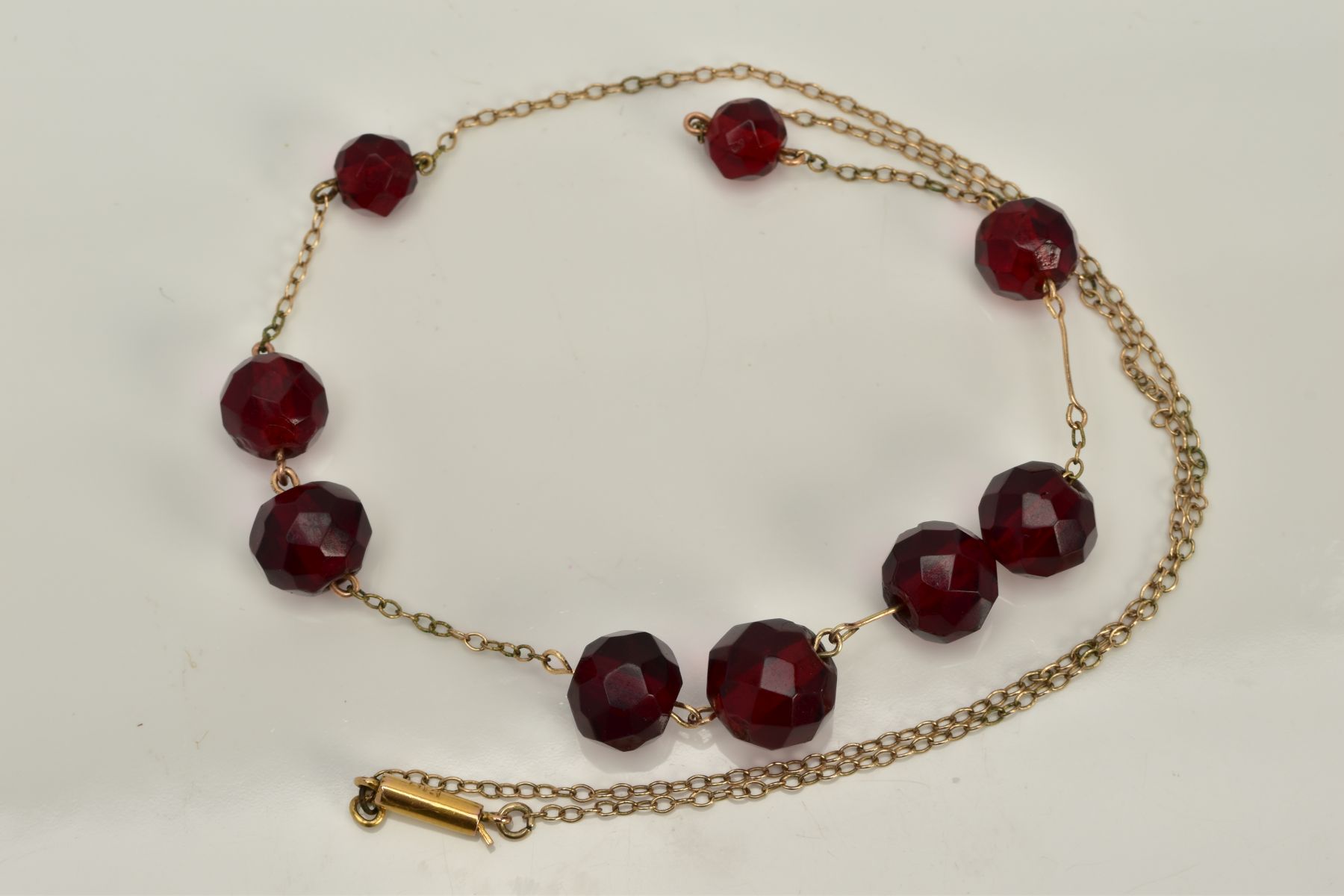A YELLOW METAL BEADED NECKLACE, designed with a row of nine graduated faceted red beads, assessed as