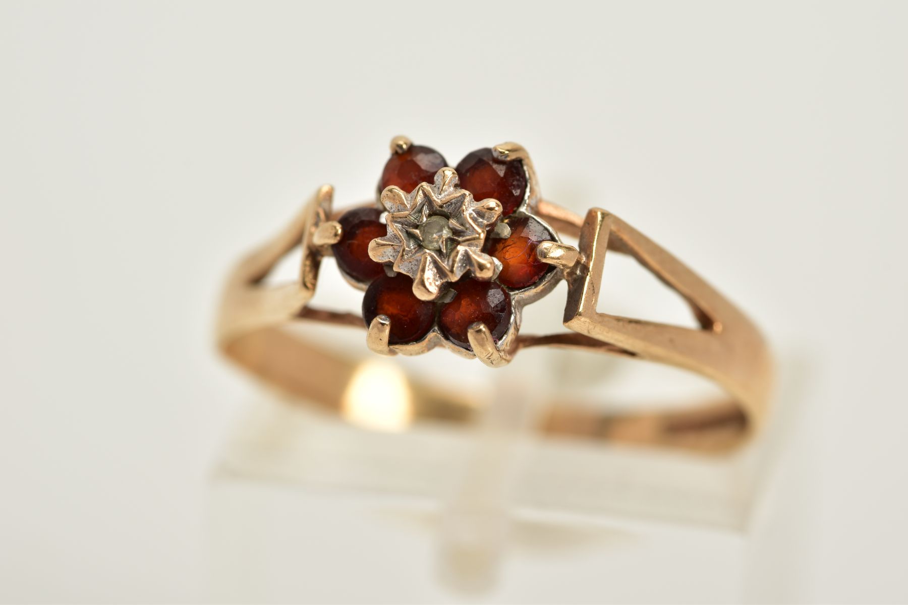 A 9CT GOLD GARNET AND DIAMOND CLUSTER RING, designed with a central single cut diamond, circular cut