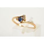 A SAPPHIRE AND DIAMOND YELLOW METAL RING, of cross over design set with an oval cut sapphire flanked