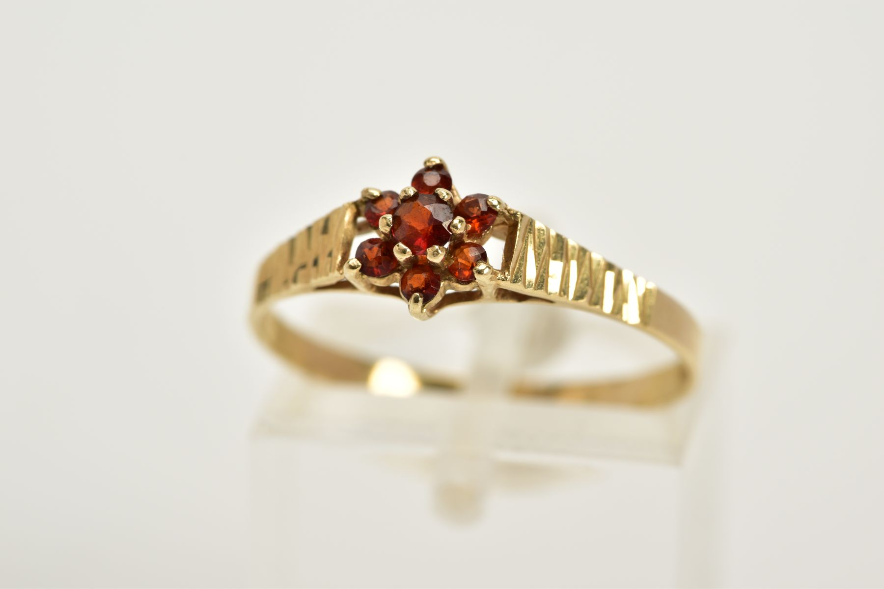 A 9CT GOLD GARNET CLUSTER RING, designed with a small central cluster set with seven circular cut