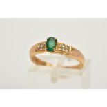 AN EMERALD AND DIAMOND RING, the yellow metal ring set with a central oval cut emerald, flanked with
