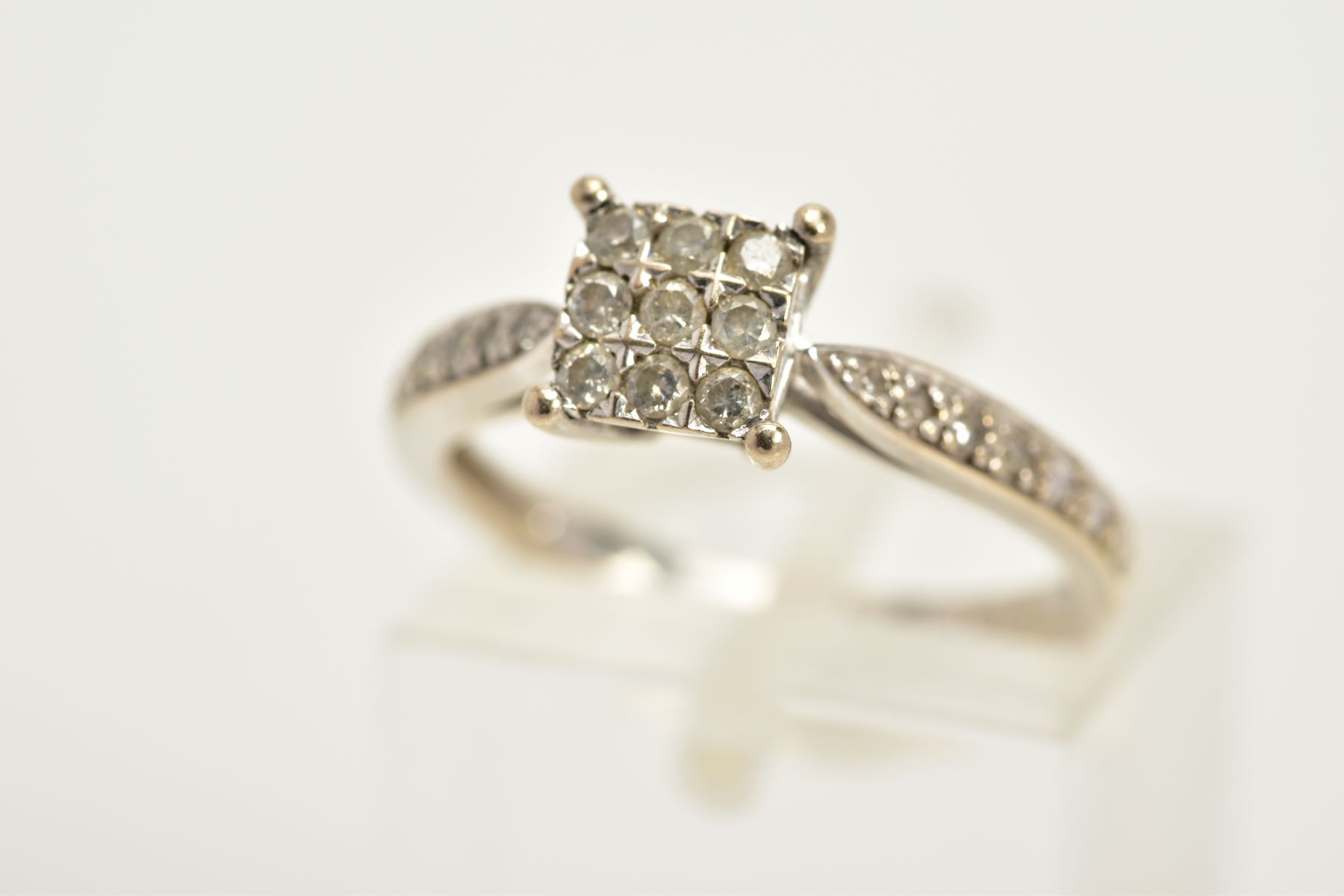 A WHITE METAL DIAMOND RING, the square central panel set with nine round brilliant cut diamonds,