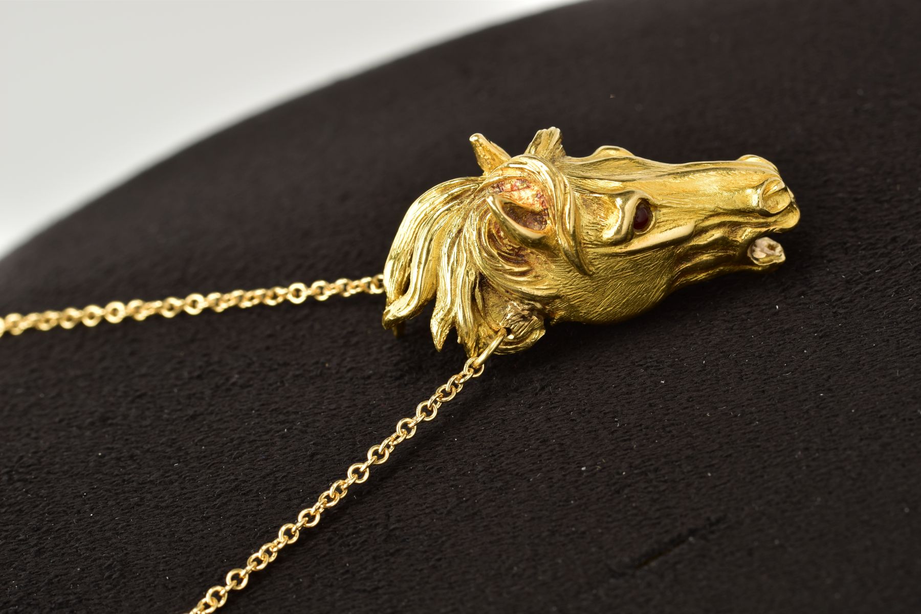 A MODERN HORSE HEAD PENDANT, realistically stylized, textured finish with ruby eyes, pendant