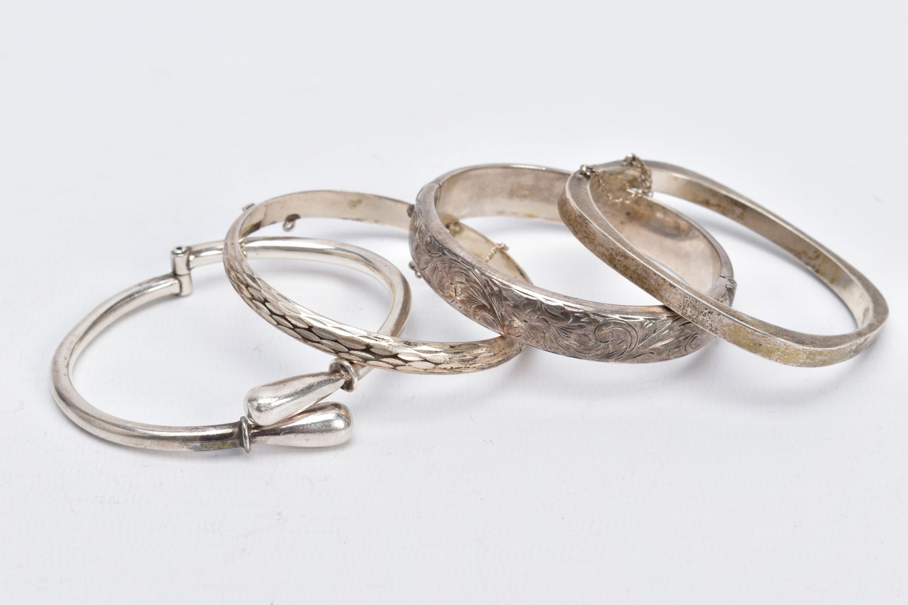FOUR SILVER BANGLES, such as a floral engraved hinged bangle, with broken safety chain, hallmarked