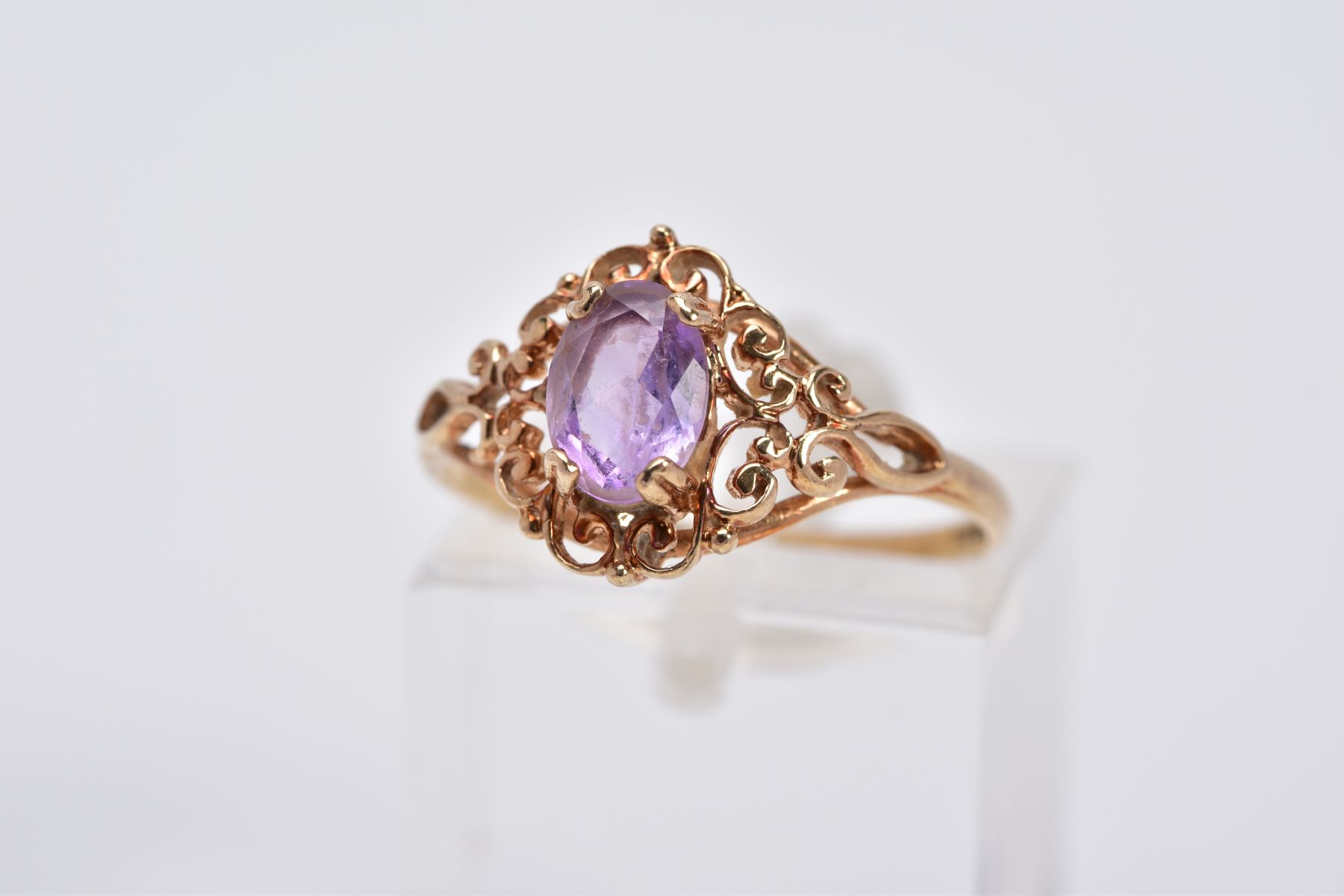 A 9CT GOLD AMETHYST RING, designed with a claw set, oval cut amethyst, within an openwork scroll