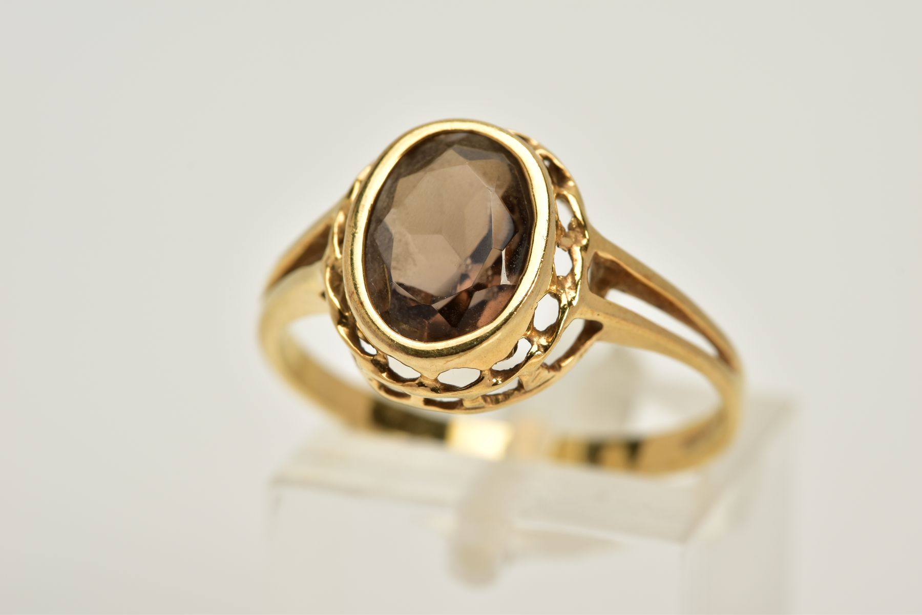 A 9CT GOLD SMOKEY QUARTZ RING, designed with an oval cut smokey quartz within a collet mount,