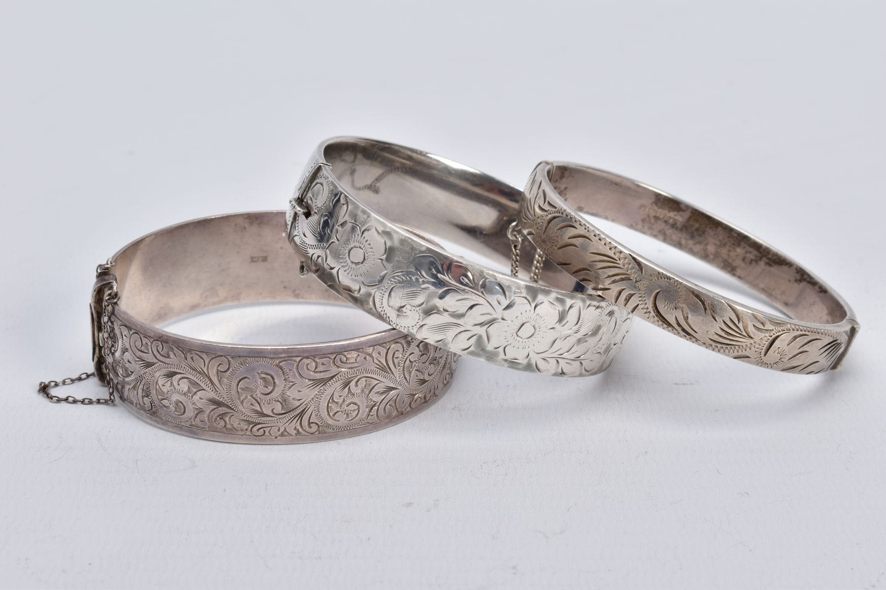 THREE SILVER HINGED BANGLES, the first a wide bangle with a foliate engrave design, push pin clasp