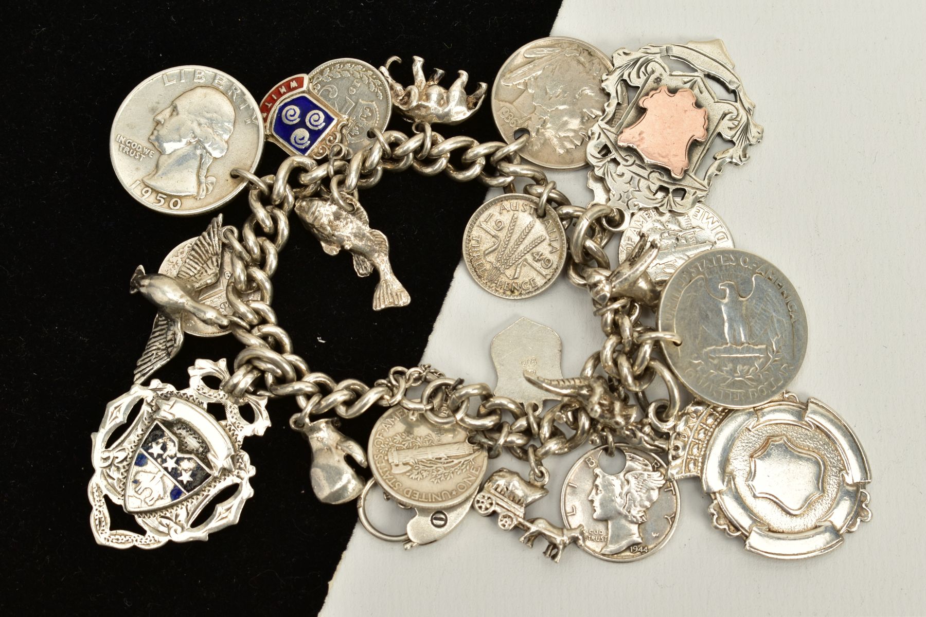 A SILVER CHARM BRACELET, suspending twenty-three charms, such as coins, fobs, a dog, crocodile,