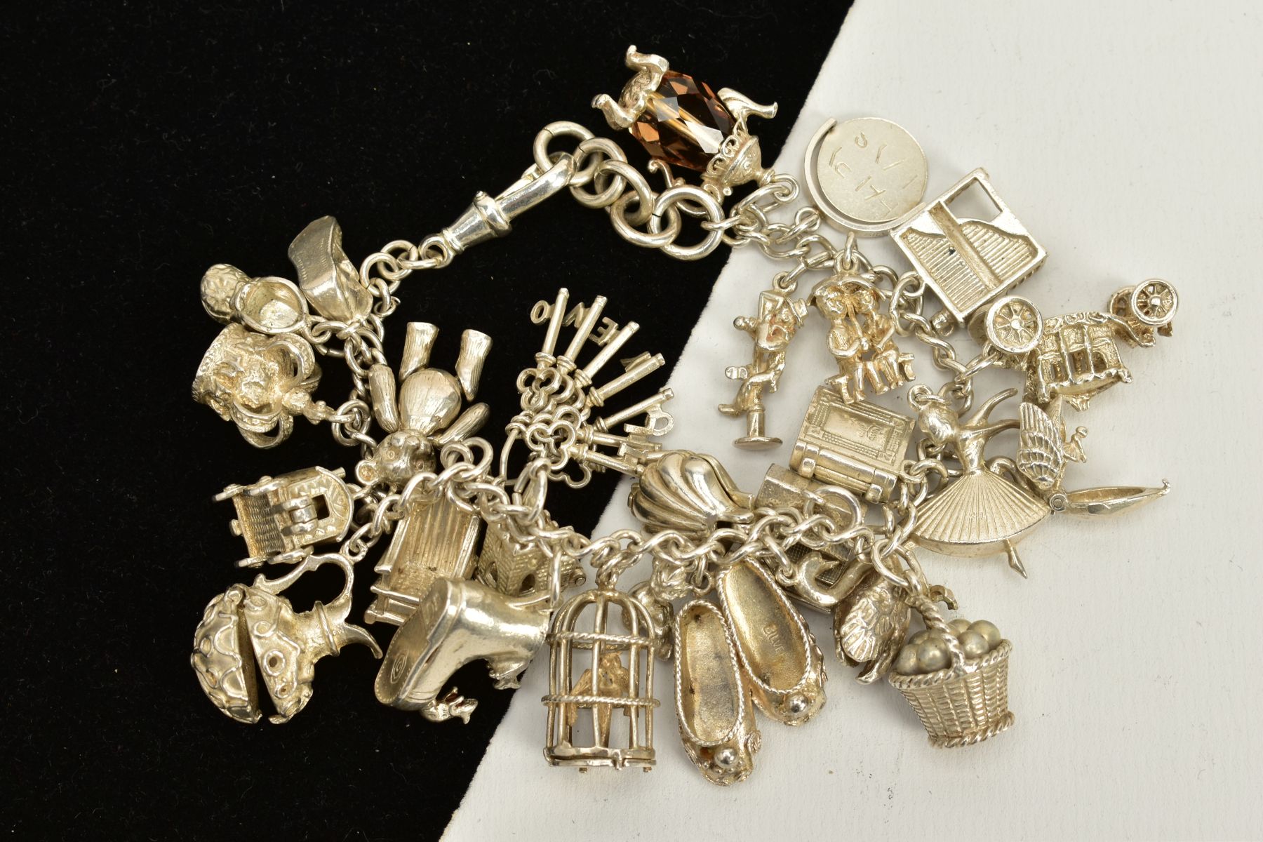 A CHARM BRACELET, suspending twenty five charms in forms such as a bird in a cage, ballerina