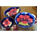 THREE MOORCROFT POTTERY PIN DISHES, all with a red/purple hibiscus on a blue ground, one an oval,