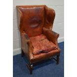 A DISTRESSED EARLY 20TH CENTURY COPPER ORANGE WING BACK ARMCHAIR on a mahogany frame (sd and