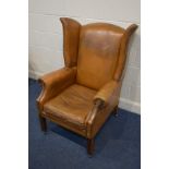 A TAN LEATHER WING BACK ARMCHAIR, on mahogany legs, along with later cushions, width 77cm (worn