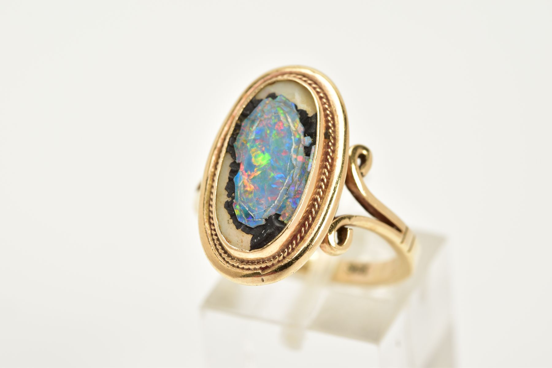 A YELLOW METAL RING, of oval design, set with a broken opal triplet, within a collet mount and