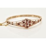 A 9CT GOLD GARNET SET OPENWORK BANGLE, the openwork hinged bangle of floral design, set with