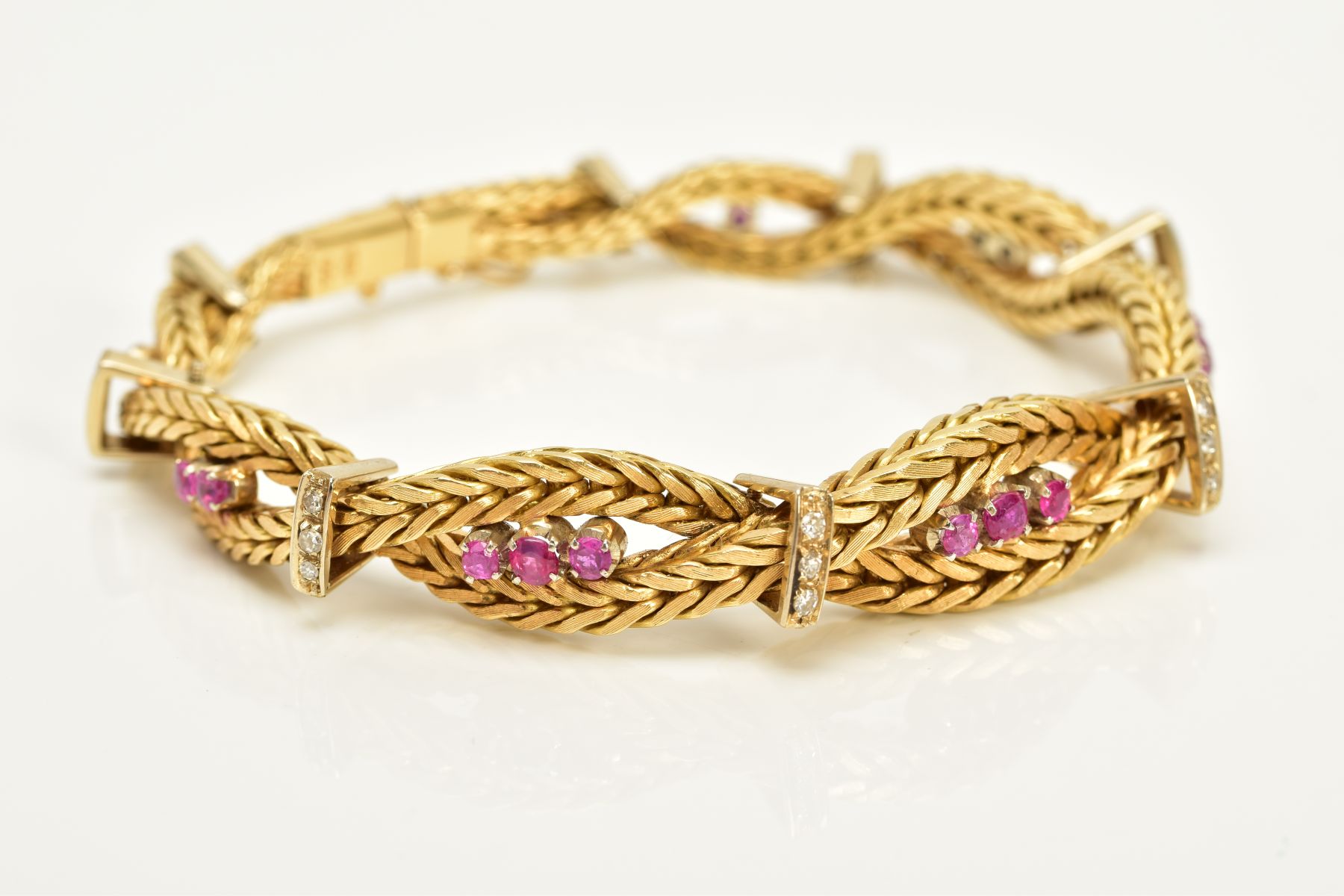 A MODERN YELLOW METAL DIAMOND AND RUBY BRACELET, designed as a twisted box chain bracelet, seven