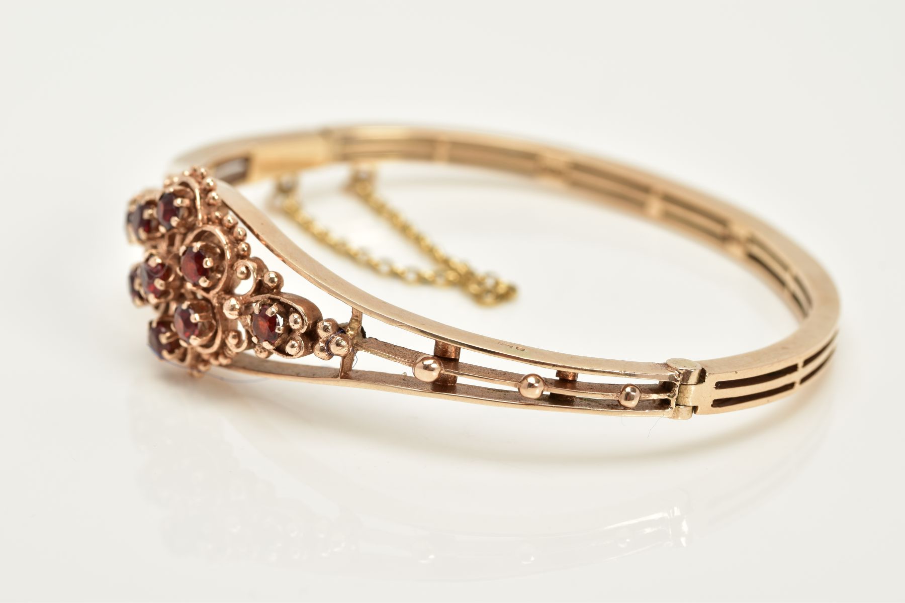 A 9CT GOLD GARNET SET OPENWORK BANGLE, the openwork hinged bangle of floral design, set with - Image 3 of 6