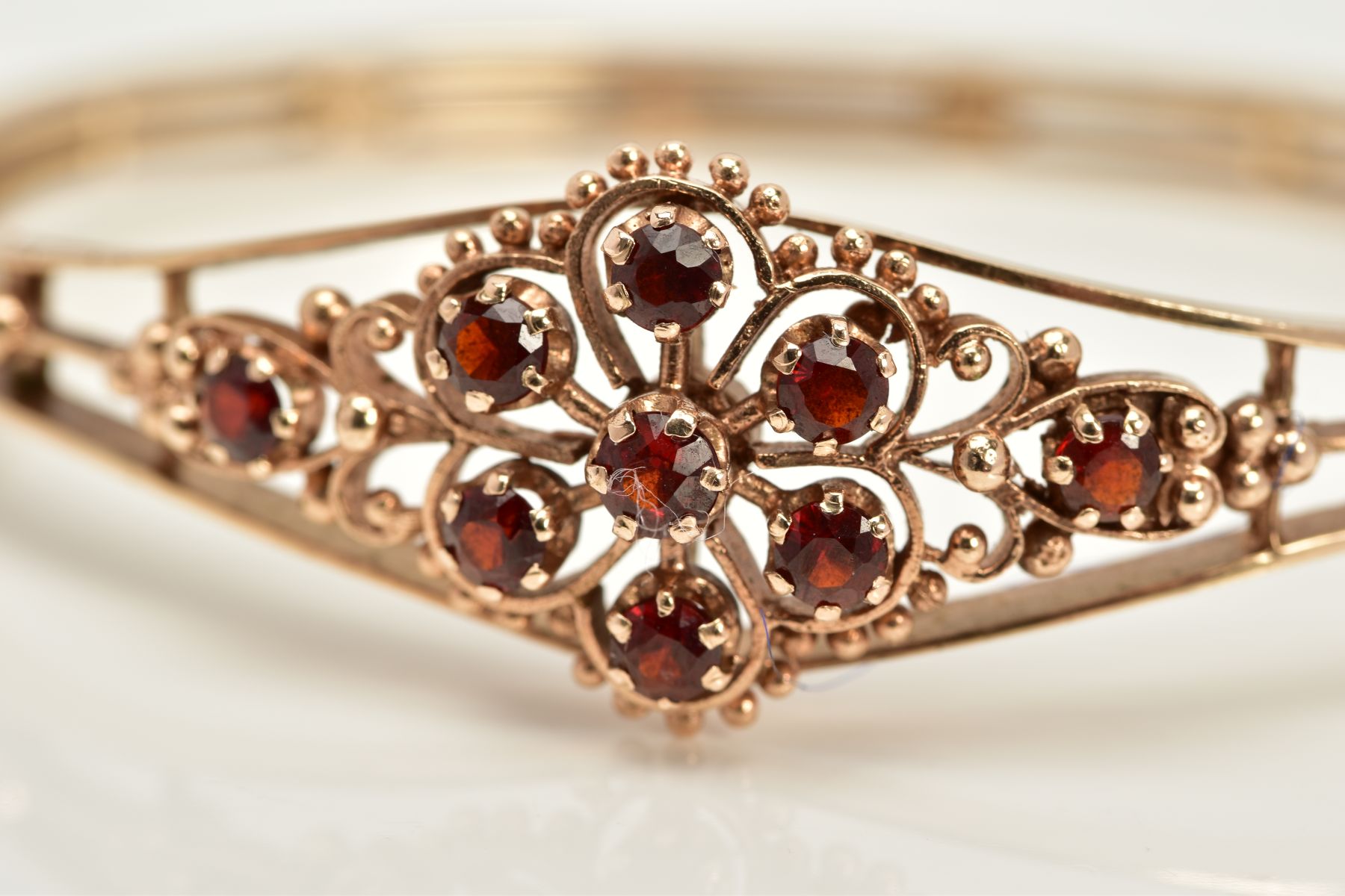 A 9CT GOLD GARNET SET OPENWORK BANGLE, the openwork hinged bangle of floral design, set with - Image 6 of 6