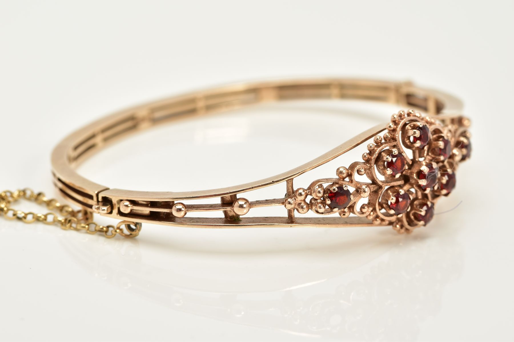 A 9CT GOLD GARNET SET OPENWORK BANGLE, the openwork hinged bangle of floral design, set with - Image 2 of 6