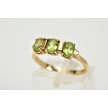 A 9CT GOLD THREE STONE RING, designed with a row of three oval cut peridots, each interspaced with a