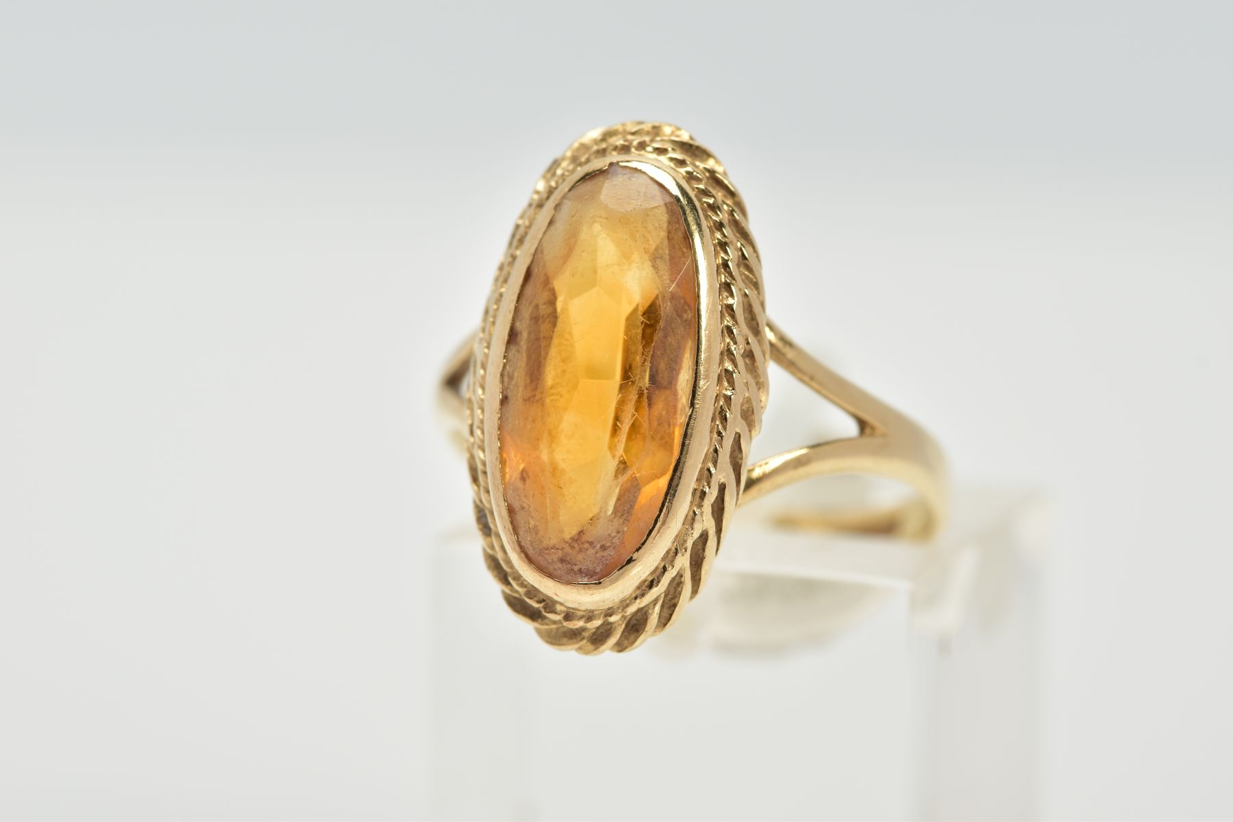 A 9CT GOLD CITRINE RING, designed with an oval cut citrine, within a collet mount and rope twist