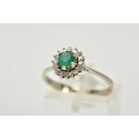 A WHITE METAL EMERALD AND DIAMOND CLUSTER RING, designed with a central circular cut emerald