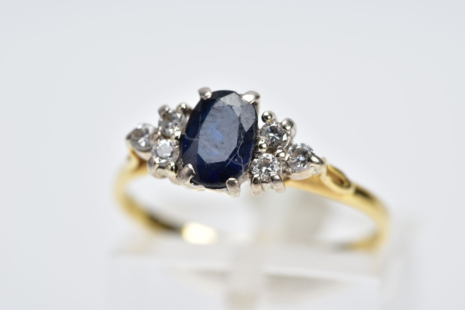 A SAPPHIRE AND DIAMOND RING, the yellow metal ring designed with an oval cut sapphire, flanked