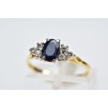 A SAPPHIRE AND DIAMOND RING, the yellow metal ring designed with an oval cut sapphire, flanked