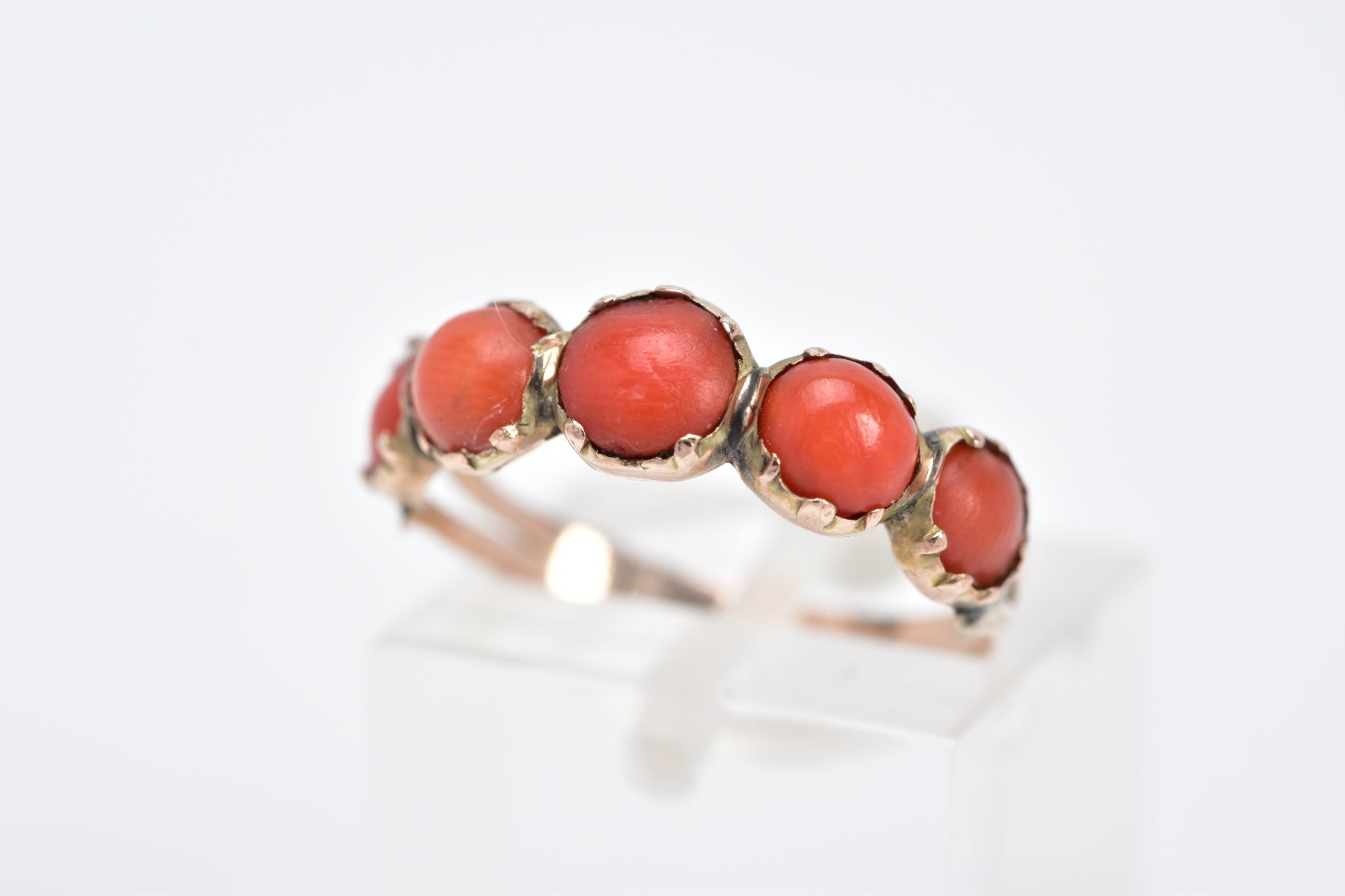 A YELLOW METAL CORAL RING, designed with five graduated coral cabochons, bifurcated textured