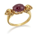 A ruby single stone ring, the oval cabochon ruby in claw -set mount between single skull motifs,