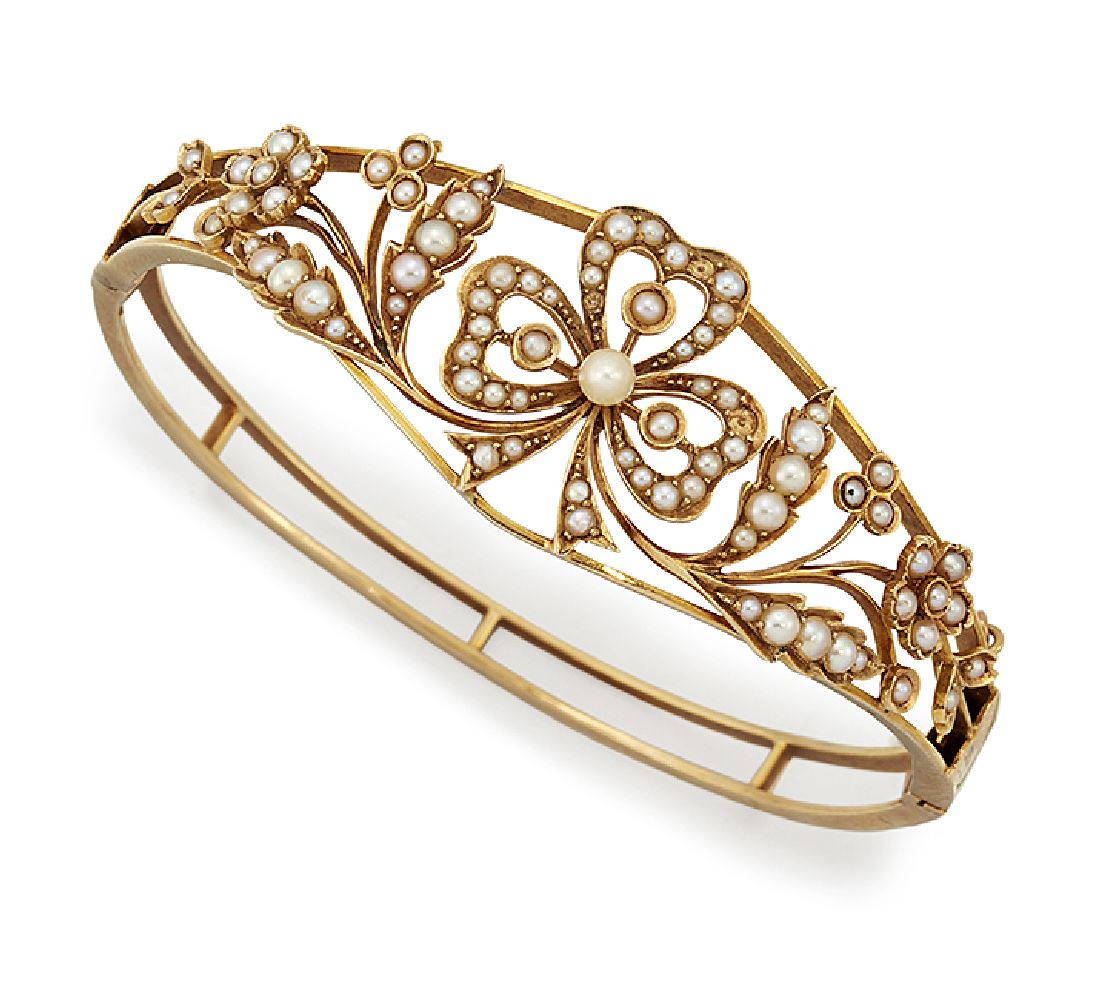 An Edwardian gold and half-pearl bangle, of hinged open hoop design, the tapered front with