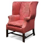 A George III wingback armchair, with serpentine wings, upholstered in red floral pattern fabric,