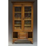 An Arts and Crafts oak bookcase, the moulded cornice above two leaded and stained glass doors,