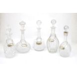 Five glass decanters, one with silver collar, and five silver labels200