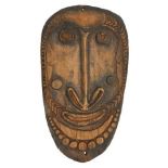 An oval tribal hardwood shield, 20th century, carved with a face within a beaded border, 95 x