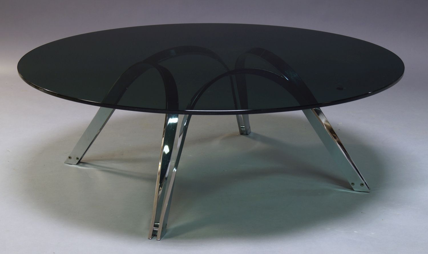 A modern chrome coffee table, c.1980, with circular tinted glass top, on curved chrome supports,