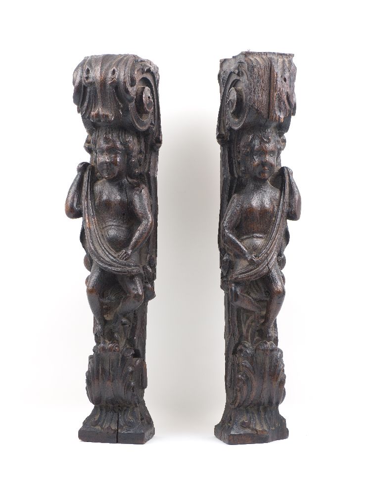 A pair of 17th century carved oak corbels, each designed as a putto holding drapery, in a surround