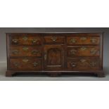 A George III oak dresser base, with seven drawers about a central cupboard door, raised on bracket